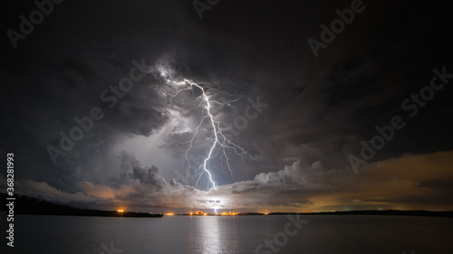 View of lightning over factory with ocean in foreground at night