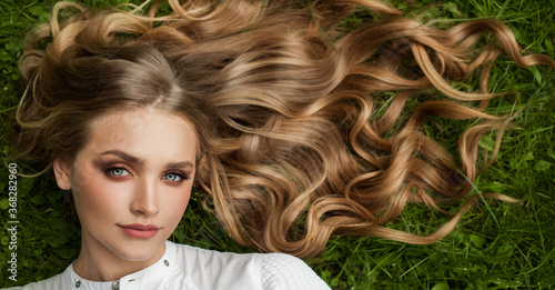 Beautiful blonde woman with long curly hair and healthy skin on green grass outdoor, top view photo