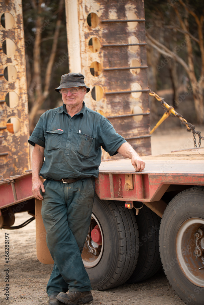 Older worker in dark green workwear standing next to truck Older worker in dark green workwear standing next to truck