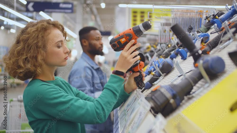 Young woman choosing electric screwdriver in hardware store
