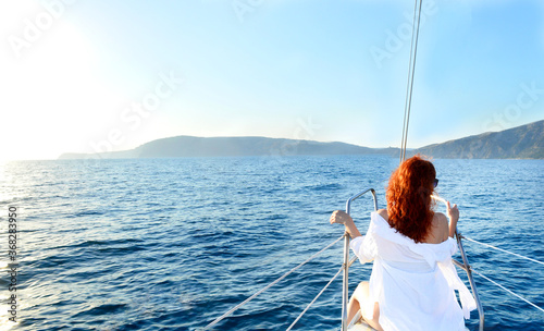 Back view of a young woman with red hair in a white shirt sits on the yacht. Crimea, Black Sea, Balaklava. The concept of rest, travel, cruise, vacation. Banner. copy space.