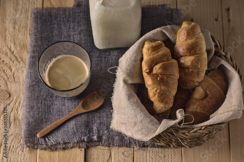 croissant recién horneados sobre un cesto de mimbre en una mesa con café y leche, listo para tomar en desayuno o merienda photo