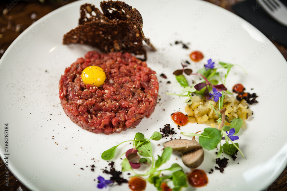 Steak tartare. Horseradish creme, black bread, baguette chips on white plate. Delicious healthy raw meat food closeup served on a table for lunch in modern cuisine gourmet restaurant. Steak tartare. Horseradish creme, black bread, baguette chips on white plate. Delicious healthy raw meat food closeup served on a table for lunch in modern cuisine gourmet restaurant.