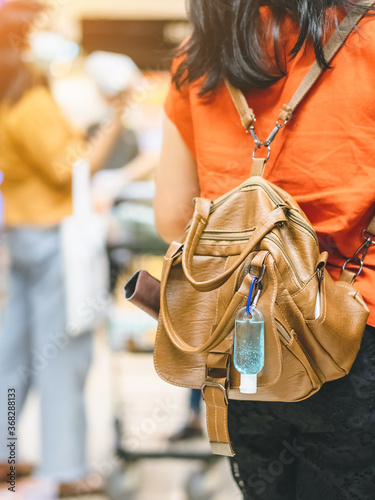 Mini portable alcohol gel bottle to kill Corona Virus(Covid-19) hang on a leather shoulder bag of a woman wearing a mask to shopping in supermarket.New normal lifestyle.Selective focus on alcohol gel