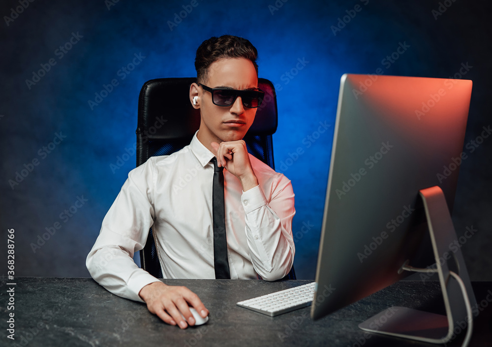 Young office man in white shirt working using computer in the office, looks pensive. Studio shot with blue and red lights