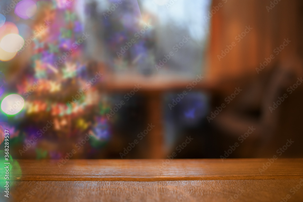 Cozy Christmas blurred background with bokeh, table, Christmas tree in living room and wooden tabletop in foreground.