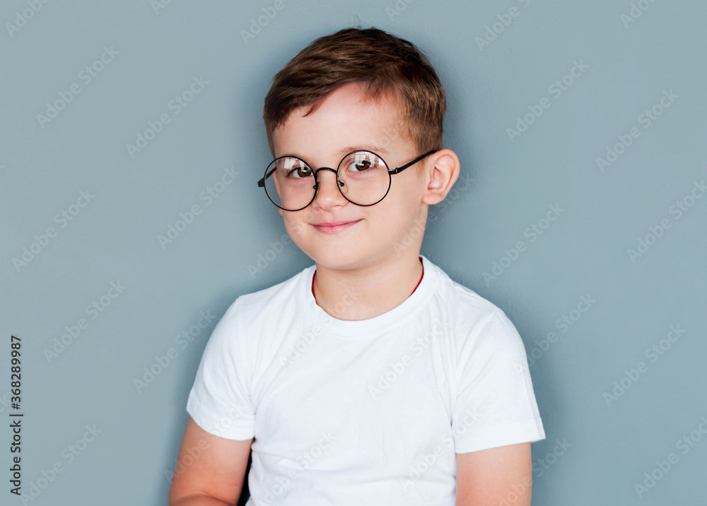 Photo of adorable young happy boy wearing white t-shirt looking at camera over grey background