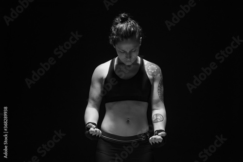 A young, female boxer with dark hair styled with a fade on one side, stands in contemplation of her next bout.  photo