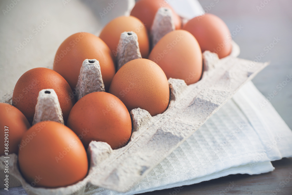 On the grey kitchen table is a white towel and a store - bought cardboard box containing a brown chicken eggs. Products of animal origin. On the grey kitchen table is a white towel and a store - bought cardboard box containing a brown chicken eggs. Products of animal origin.