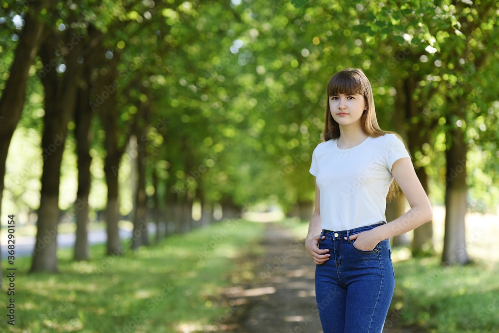 A girl stands on the road in a Park, dressed in a t-shirt and jeans.