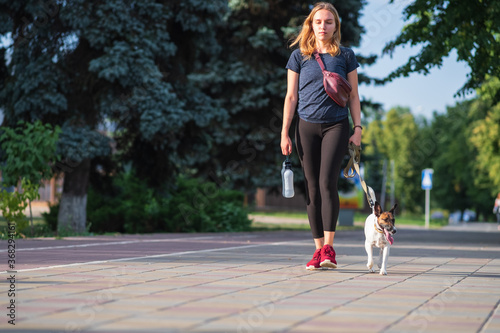 A woman walks with her dog in urban background. Having pets in town, acessories for puppies, lifestyle with dogs, smooth fox terrier breed