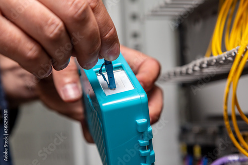 A man works with a blue fiber optical connector cleaner near a cabinet. Cleaning connectors close up. Horizontal orientation.
