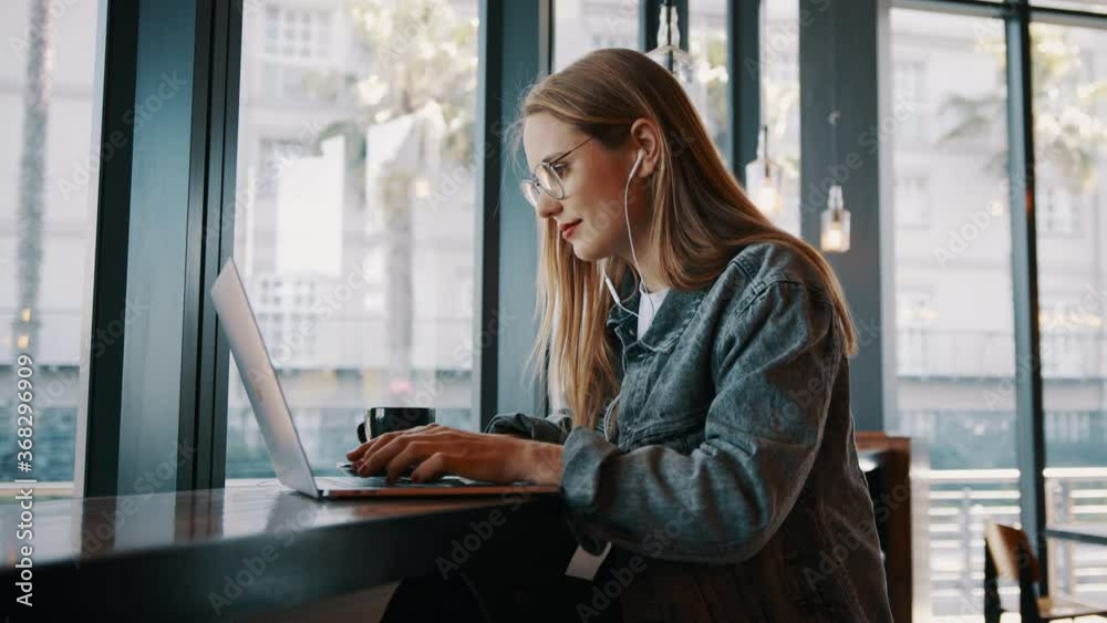 Young woman working on laptop computer at a cafe. Caucasian female influencer in a coffee shop using a laptop.
