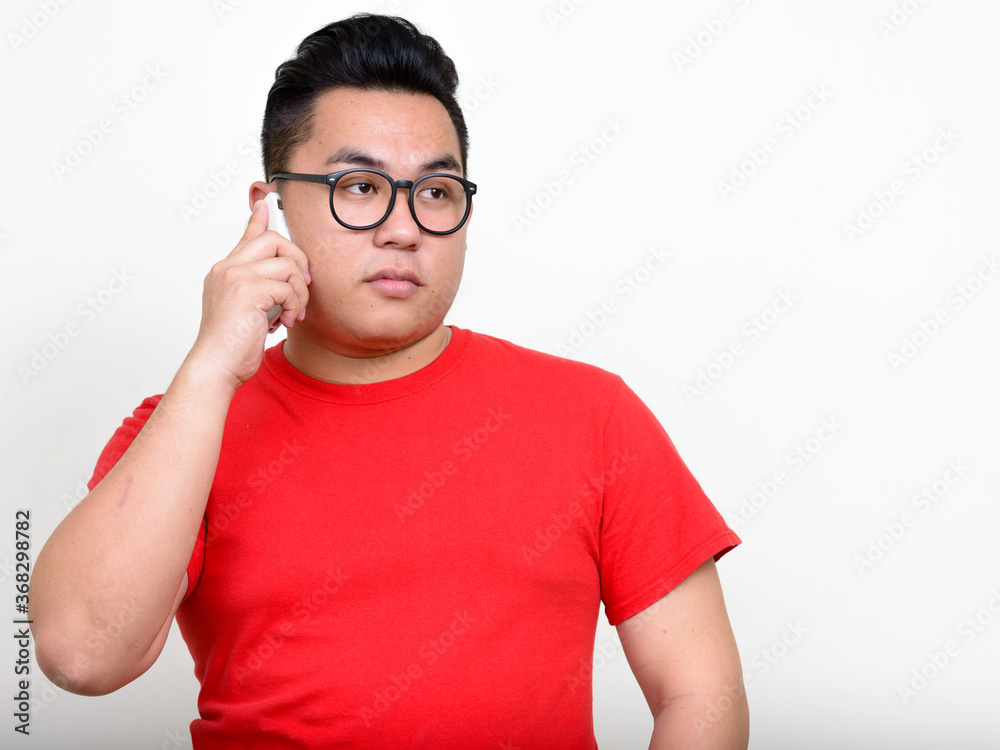 Portrait of young overweight Asian nerd man talking on the phone Portrait of young overweight Asian nerd man talking on the phone