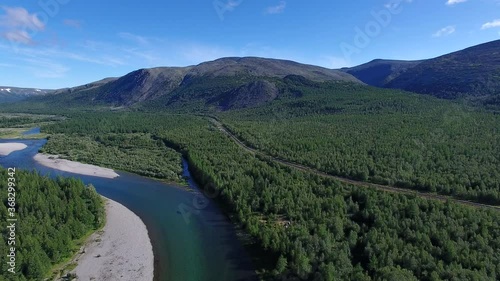 The camera flies over the valley of a mountain river. Along the river there is a railway, on the sides of the mountain