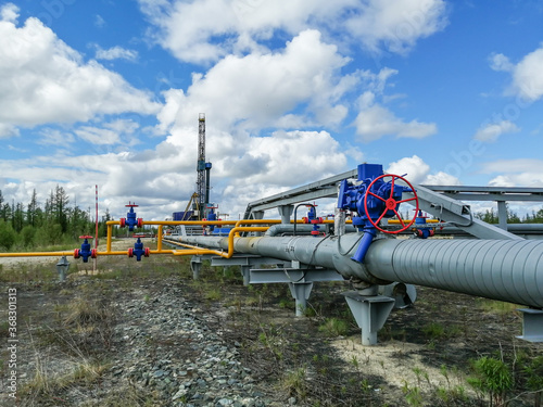 Pipeline manifold of gas wells of producing gas wells in the northern field. High pressure gate valve handwheels, pipelines. In the background, a drilling rig. Blurring distant objects.