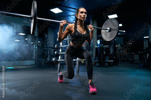 Woman doing lunges using barbell in gym.
