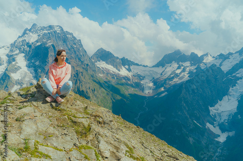 Young woman sitting on rock and looking at mountain landscape. Female traveler enjoying beautiful view in mountainous area.