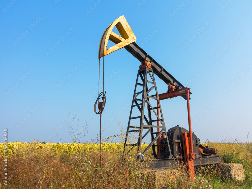 A Small private oil derrick pumps oil on the field. The old handicraft oil rig in the background of the creative industrial design.