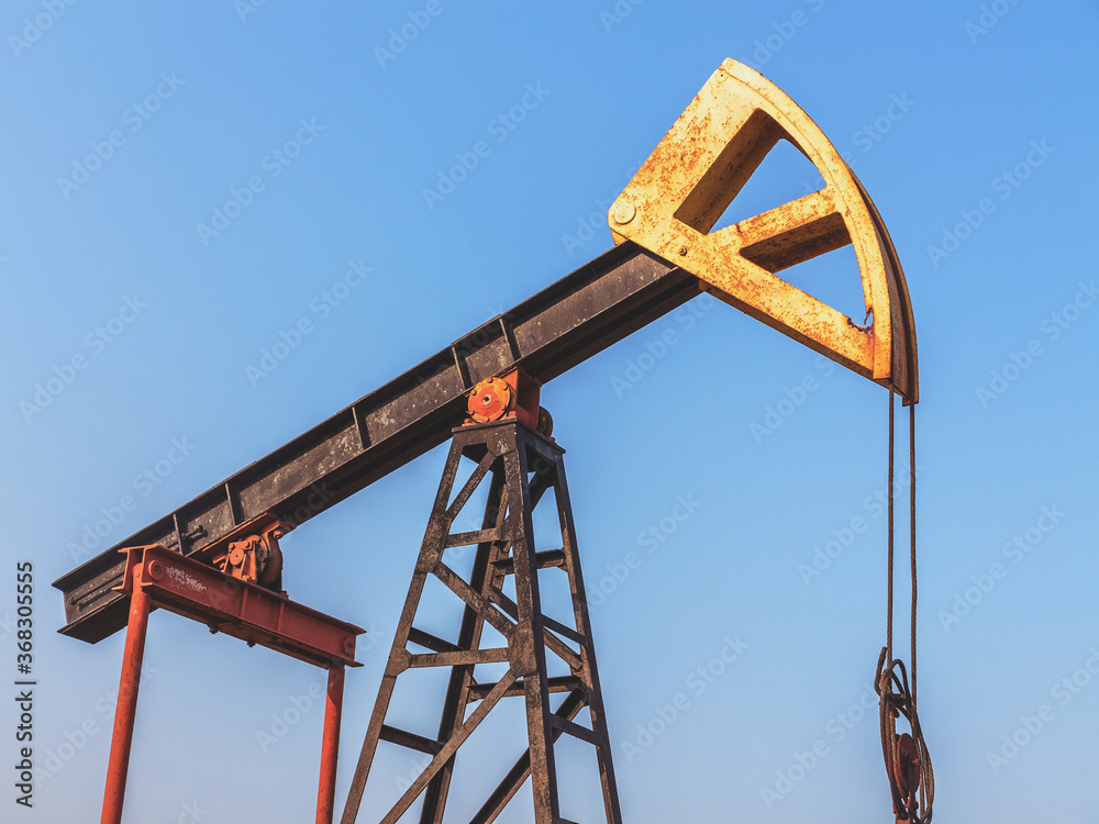 A Small private oil derrick pumps oil on the field. The old handicraft oil rig in the background of the creative industrial design. A Small private oil derrick pumps oil on the field. The old handicraft oil rig in the background of the creative industrial design.