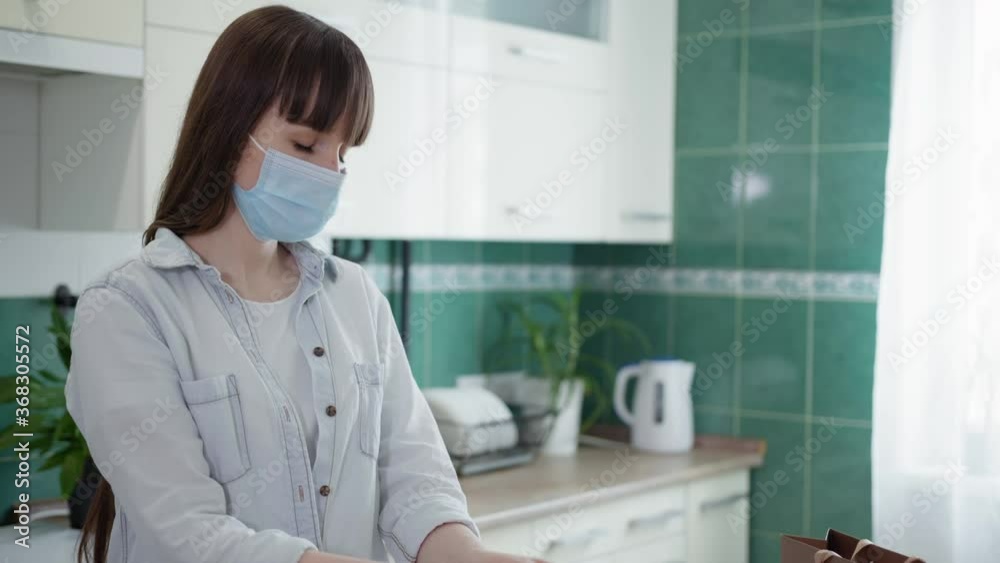adult girl in medical mask observes precautions and disinfects containers with food left by courier at home during pandemic of virus and infection adult girl in medical mask observes precautions and disinfects containers with food left by courier at home during pandemic of virus and infection