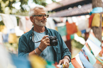 60-year old man active trekking in Nepal, photographer explores the national culture. Elderly person in travel, healthy lifestyle of pensioner.