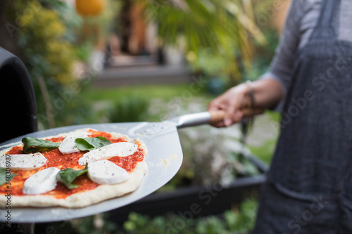 Woman cooking homemade pizza at pizza oven on patio photo