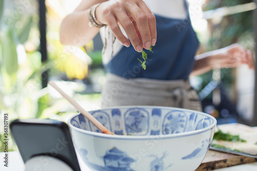 Woman sprinkling fresh herbs in bowl photo