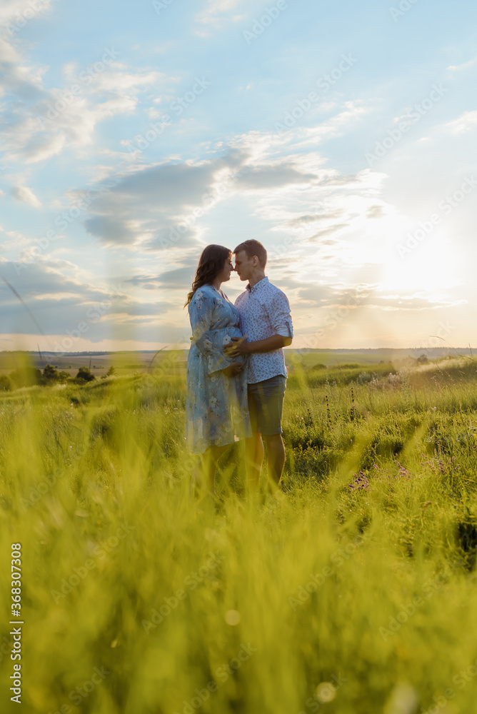 Pregnant woman holding hands with her husband during a walk in the field at sunset. Happy family and newborn.