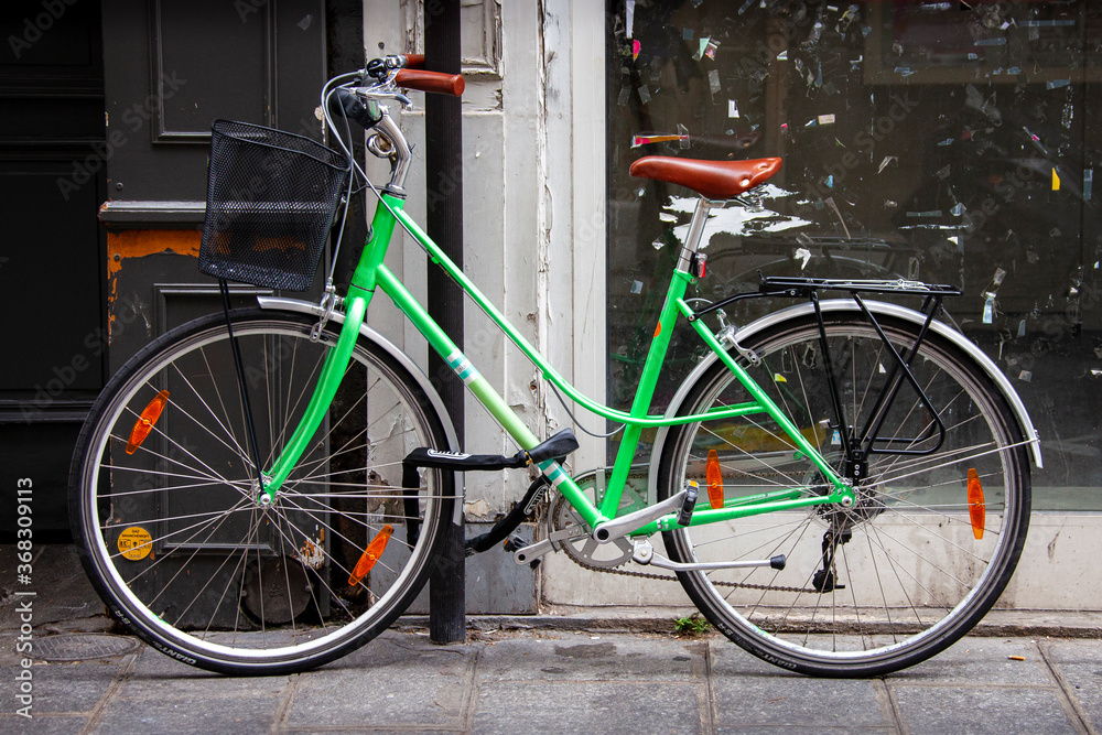 A green bicycle, one of the more popular modes of transportation in Paris, France, is chained to a pole outside an old building.