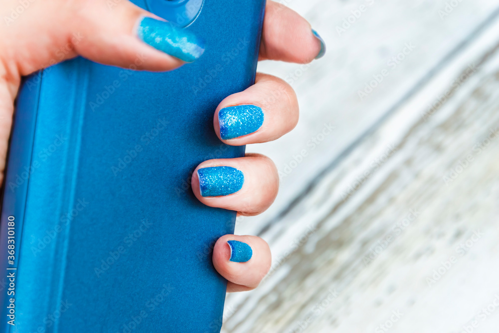 Hand holds a smartphone. Blue manicure