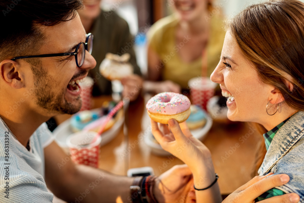 Cheerful couple having fun while eating donuts in a cafe.
