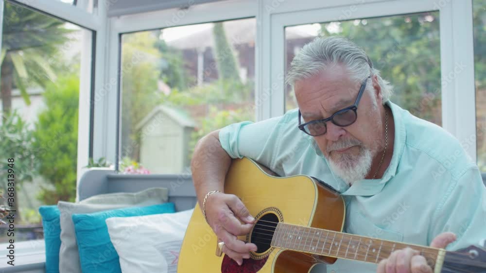 Retired senior male playing his guitar at home in his conservatory, in slow motion 