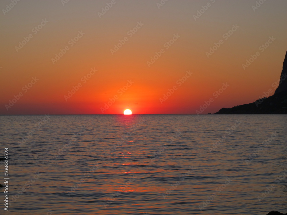 A picturesque sunset, the sun sets on the horizon in the sea. Red sunset sky, silhouettes of seagulls against the setting sun on the horizon, summer evening on the seaside