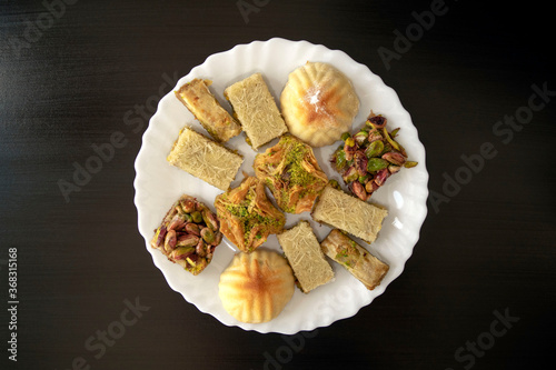 Traditional middle eastern mamoul cookies and assorted baklawa. Top view. Arabic baked sweets with nuts in white plate on dark wooden table. Ayd El Fithr feast cookies. photo