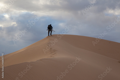 A photographer hiking up a sand dune to get a picture