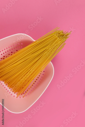 Różowy durszlak z surowym zbożowym makaronem na spaghetti bolognese na różowym tle