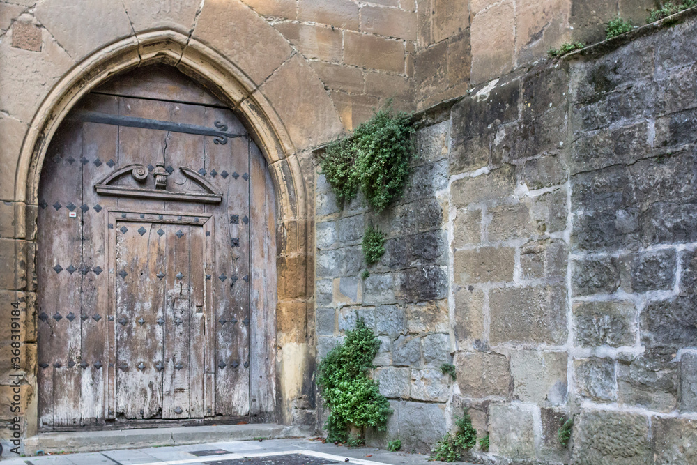 Heavy wooden door. Ancient gate on the facade of a stone building. The architecture of medieval Spain. Streets of Pamplona. Catholic Church. Massive door with a lock. Heavy wooden door. Ancient gate on the facade of a stone building. The architecture of medieval Spain. Streets of Pamplona. Catholic Church. Massive door with a lock.