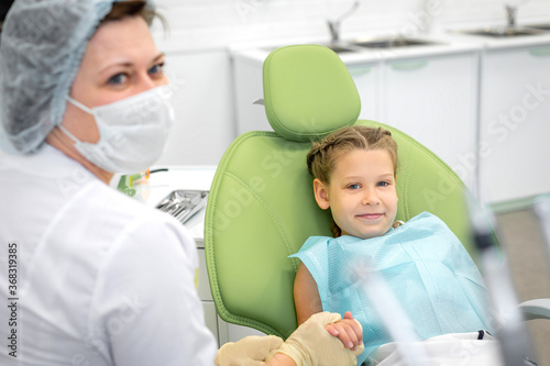 Happy caucasian kid on regular check up of teeth in dental clinic. Dentist holds a seven year old girl by her hand