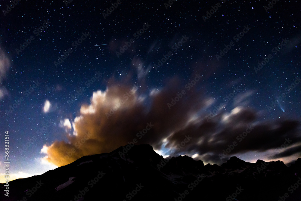 Stars and clouds in the night in italian alps, including Neowise comet on the right
