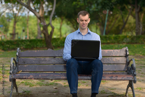 Portrait of happy businessman using laptop at the park