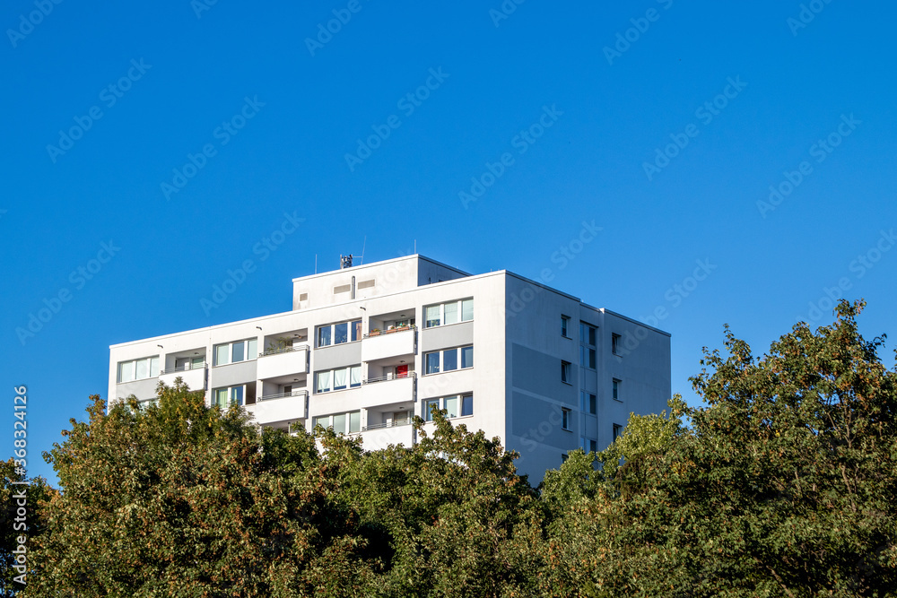 Cologne, NRW, Germany, 07 30 2020, white appartment building, behind trees, blue sky