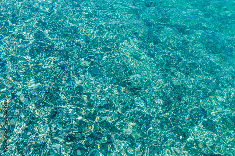 Fototapeta premium Natural background of transparent azure sea water and bottom with rocks. A close-up view of the pebbles on the beach. Blue bottom of the Mediterranean sea with small stones through clear water