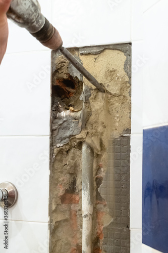 repairing of plumbing riser of heated towel rail at home - cleaning a water pipe in brick wall from concrete with rotary hammer photo