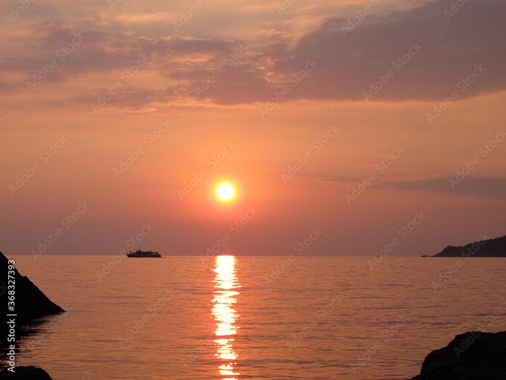 Scenic view of bright golden setting sun and reflection in sea water, silhouette of a pleasure boat on the horizon, sunset on the seaside, clouds, sky, sea and sun in orange-pink tones
