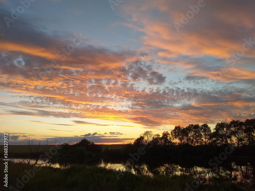 Sunset over a small river with red-lit clouds. Landscape with the sun hidden behind the horizon.