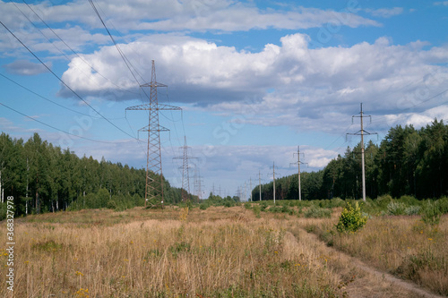 Lots of high-voltage towers and wires running between the woods, forest. Delivery of electricity to localities and cities.