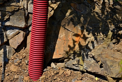 Red protective tube for electric cables on a rock. Grooved protective tube. Spiral industrial pipe. Stone background. photo