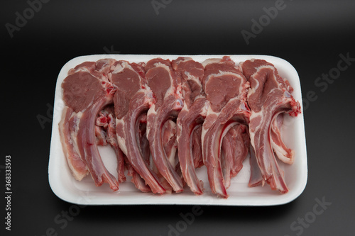 Raw lamb chops (cutlets) in a white styrofoam container isolated on black background with copy space for text