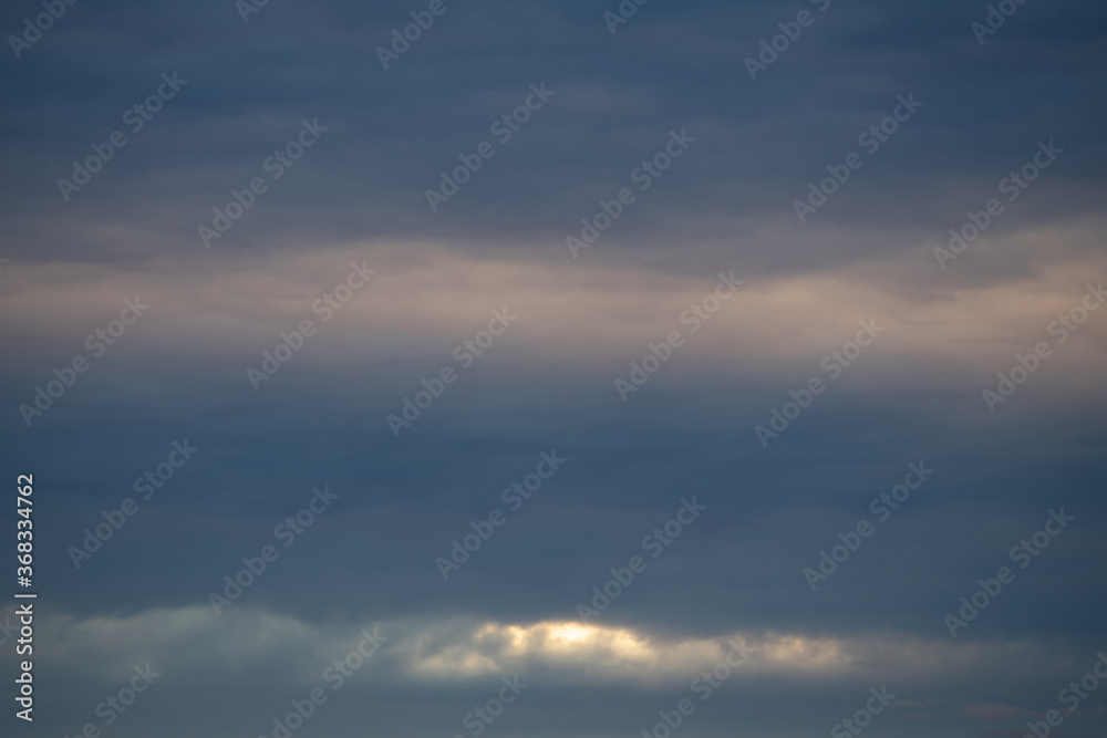 Dramatic evening sky with dark clouds and sun light in the background.